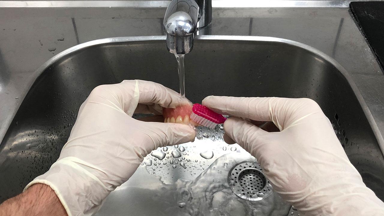 Reinigung der Prothesen mit Zahnbürste unter fließendem Wasser.